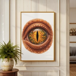 Puede incluir: Una impresión enmarcada que presenta una ilustración detallada de un ojo de reptil. El ojo tiene un iris dorado con intrincados patrones verdes y amarillos, rodeado de escamas texturizadas de color marrón rojizo. La obra de arte está sobre un fondo blanco.