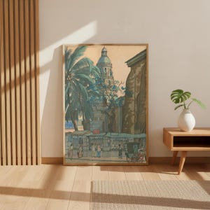 Op de afbeelding: Ingelijste vintage prent die een straatbeeld toont met een kerk en palmbomen. Het kunstwerk gebruikt gedempte tinten blauw, groen en beige, met figuren en een paardenkoets. De prent wordt weergegeven in een houten lijst.