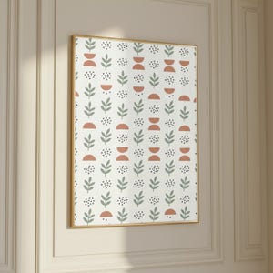 May include: A framed art print featuring a repeating pattern of stylized leaves, half-circles, and small black dots on a white background. The leaves are a muted green, and the half-circles are a terracotta color. The frame is gold.