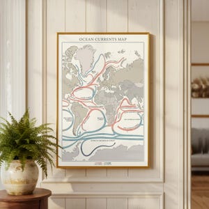 May include: Framed world map print titled "Ocean Currents Map." The map features a neutral color palette with red and blue lines indicating ocean currents. The map is encased in a gold frame and hangs on a white wall.