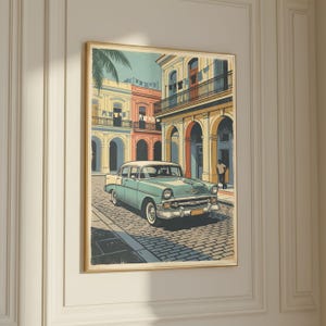 May include: A framed print of a vintage car on a cobblestone street in a colorful city. The car is light blue and white, and the buildings are yellow, orange, and pink. A palm tree and a person are also visible.
