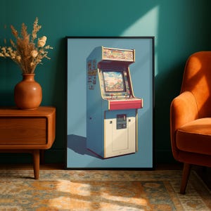 May include: A framed wall art print featuring a light blue arcade cabinet with a screen, control panel, and coin slot. The cabinet has a red accent panel below the screen and a marquee at the top. The artwork is displayed in a black frame.