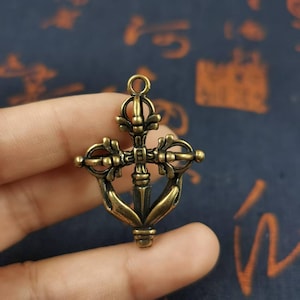 May include: Bronze pendant with an intricate design. The pendant has a central vertical element with a cross-like shape, with curved arms and circular details. It has a loop at the top for hanging.