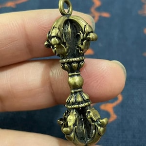 May include: A detailed bronze-colored pendant with intricate floral and geometric designs. The pendant has a loop at the top for hanging and a symmetrical shape. The overall design is ornate and detailed, with a vintage aesthetic.