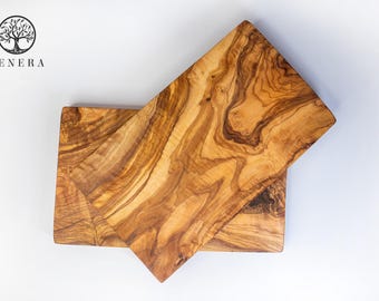 May include: Two rectangular olive wood cutting boards, one stacked on top of the other. The boards have a natural wood grain pattern with a light brown color.