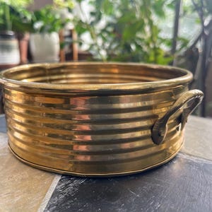May include: A gold-colored metal coaster with a ribbed design and a single handle. The coaster is round and has a shiny finish.