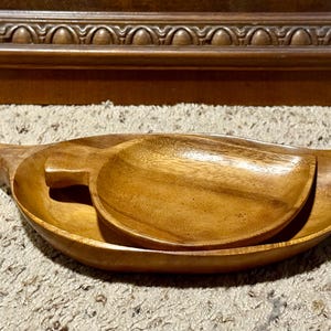 May include: A wooden serving tray with a handle and a smaller, matching dish nested inside. The tray and dish are made of light brown wood and have a smooth finish. The tray is approximately 12 inches long.