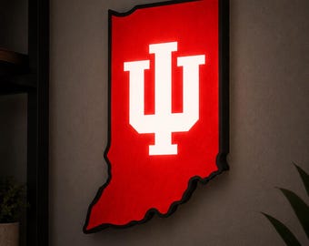 May include: A wall-mounted, illuminated sign shaped like the state of Indiana. The sign features a vibrant red background with a bold, white, block-style IU logo centered in the middle. The entire piece is framed by a thin, black border.
