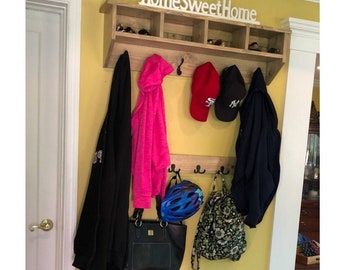 May include: A wooden entryway bench with two shelves for storing shoes. The bench has a coat rack above it with hooks for hanging coats, hats, and bags. The coat rack has a shelf above it with the words "Home Sweet Home" written on it.