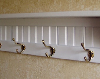 May include: White wooden shelf with four brass hooks. The shelf has a decorative slatted design.