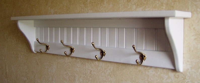 May include: White wooden shelf with four brass hooks. The shelf has a decorative slatted design.