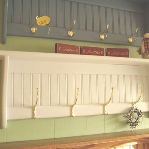 May include: White wooden coat rack with five gold hooks. The rack has a shelf with three small red signs that read "Warm", "Winter", and "Wishest".