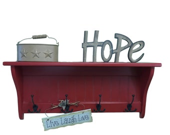 May include: A red wall shelf with four black hooks, a decorative metal container with star cutouts, and a wooden "HOPE" sign. A small sign below the hooks reads "Live Laugh Love".