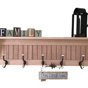 Może przedstawiać: Drewniany wieszak na ubrania z półką i pięcioma haczykami. Półka ma tabliczkę z napisem "Live Laugh Love" i drewniane klocki układające się w słowo "FAMILY".