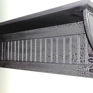 May include: Black wooden shelf with a distressed finish. The shelf has a series of vertical slats and a decorative edge.