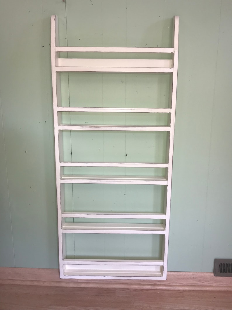 May include: White wooden shelf unit with seven shelves. The shelf unit is standing against a light green wall.
