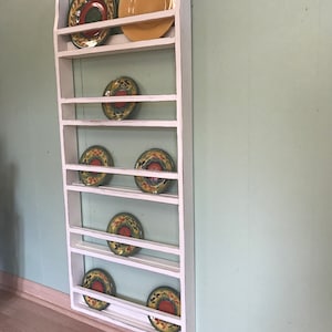 May include: White wooden plate rack with seven shelves holding colourful plates with floral designs.