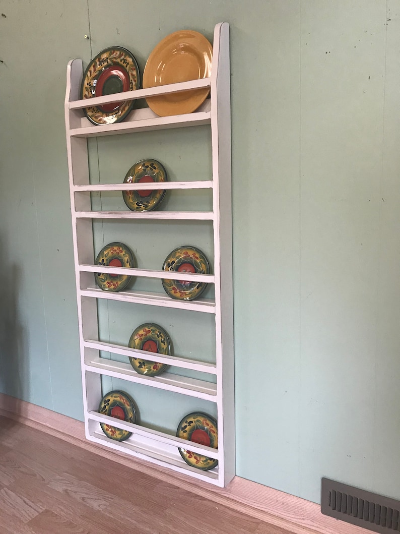 May include: White wooden plate rack with seven shelves holding colourful plates with floral designs.