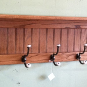 May include: A wooden coat rack with a shelf and eight hooks. The rack is stained a dark brown color and has a beaded board back.