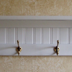 May include: White wooden shelf with four gold hooks. The shelf has a decorative, vertical, grooved design.