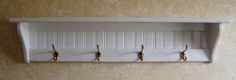 May include: White wooden shelf with four gold hooks. The shelf has a decorative, vertical, grooved design.