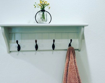 May include: White shelf with four hooks and a small vase with yellow flowers on top. A brown towel hangs from one of the hooks.