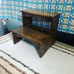 May include: A dark brown wooden step stool with two steps. The stool is made of solid wood and has a natural finish.