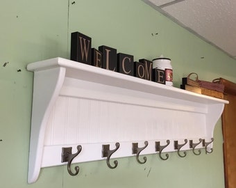 May include: White wooden coat rack with a shelf and six hooks. The shelf has a decorative trim and the word "WELCOME" spelled out in black wooden blocks.
