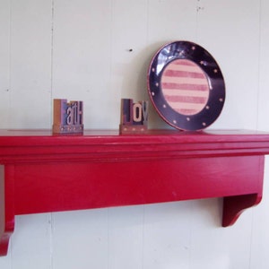 Puede incluir: Una estanter&iacute;a de madera roja con un borde decorativo. La estanter&iacute;a est&aacute; montada en una pared blanca y tiene un plato rayado azul y blanco con estrellas, y dos bloques de madera que deletrean "faith" y "joy" en la parte superior.