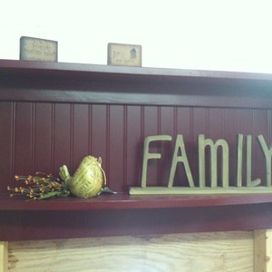 May include: A dark red wooden shelf with a scalloped edge. The shelf has a white beadboard back and a small shelf on the bottom. The shelf is decorated with a bird figurine, a small bouquet of dried flowers, and the word "FAMILY" in gold letters.