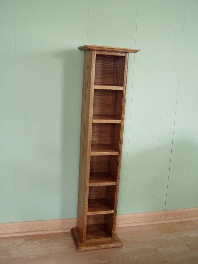 May include: A wooden DVD or CD storage tower with five shelves. The tower is made of light brown wood with a natural wood grain finish.