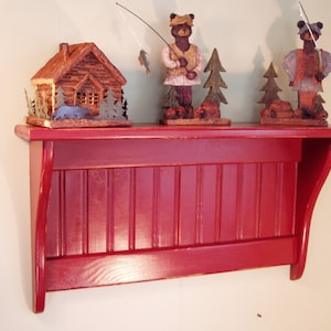 May include: A red wooden shelf with a scalloped edge and vertical slats. The shelf is decorated with three wooden figurines of bears and a small wooden cabin.