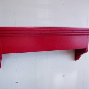Puede incluir: Un estante de madera rojo con una moldura decorativa alrededor del borde superior y un soporte curvo a cada lado.