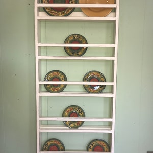 May include: White wooden plate rack with seven shelves, holding colourful ceramic plates with floral designs.