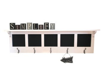May include: White wooden shelf with four black chalkboard squares and five silver hooks. The shelf has a decorative sign that says "Simplify" above the chalkboard squares. A small arrow sign with the text "Baby,  Come" hangs from one of the hooks.