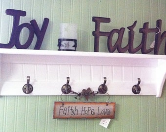 May include: White shelf with four hooks and a sign that reads "Faith Hope Love". The shelf has two wooden signs above it, one that reads "Joy" and the other that reads "Faith".