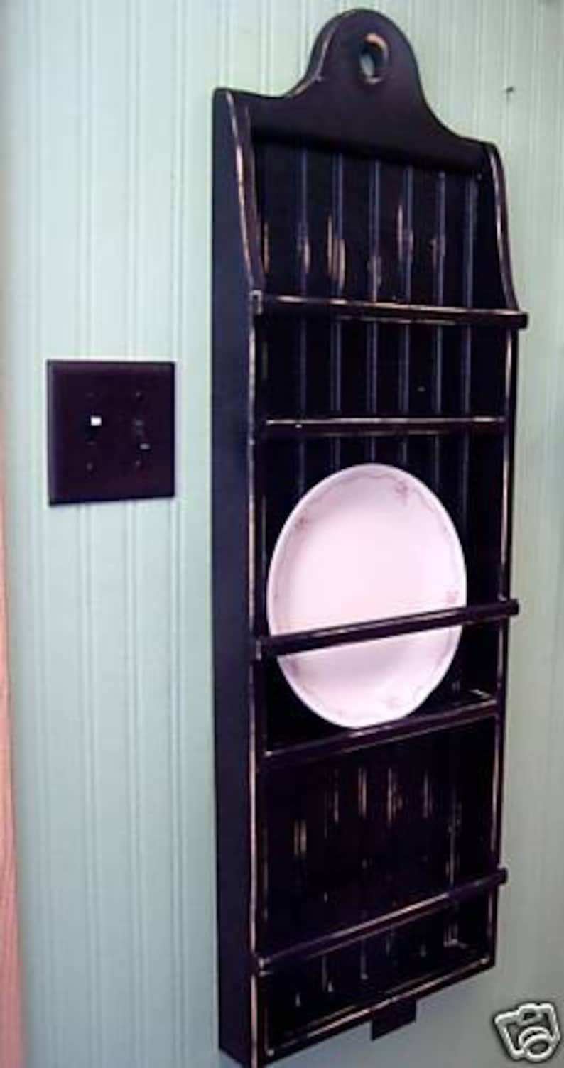 May include: Black wooden wall mounted plate rack with five shelves and a towel bar. The rack has a distressed finish and is ideal for storing and displaying plates.