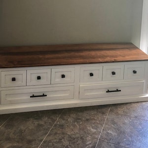 May include: White wooden storage bench with a brown wood top and six drawers. The drawers have black metal pulls.