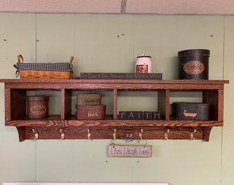 May include: A dark brown wooden shelf with four cubbies and a row of hooks underneath. The shelf is decorated with various items, including a basket, boxes, and signs. The signs read "For Ever & For Always, No Matter What", "Country", "Bath", "FAITH", and "Live Laugh Love".
