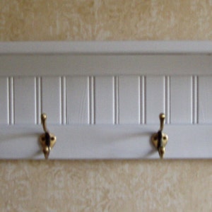 May include: White wooden shelf with four gold hooks. The shelf has a decorative, vertical slat design.