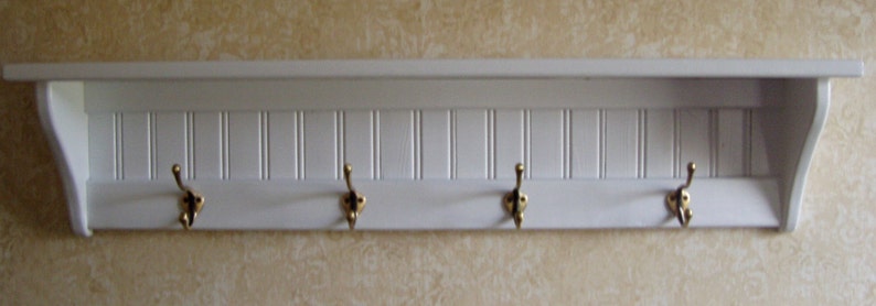 May include: White wooden shelf with four gold hooks. The shelf has a decorative, vertical slat design.