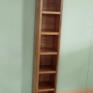 May include: A tall, wooden DVD storage tower with six shelves. The tower is made of a light brown wood with a natural finish.