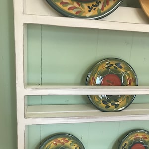 May include: White wooden plate rack with four shelves, displaying colourful patterned plates with green, yellow, and red accents.