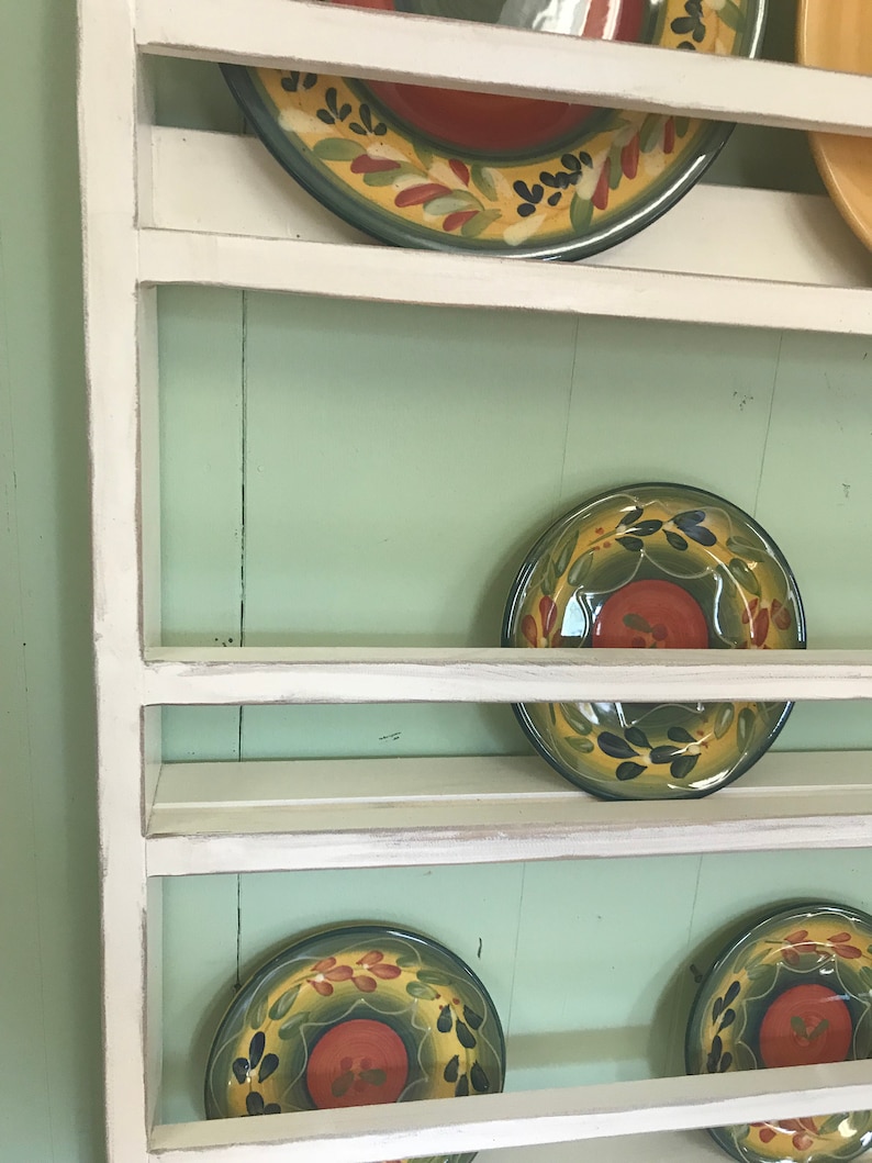 May include: White wooden plate rack with four shelves, displaying colourful patterned plates with green, yellow, and red accents.