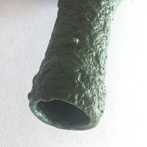 May include: A green ceramic vase with a rough, textured surface. The vase has a wide opening at the top and a narrow base.