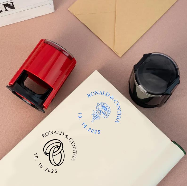 May include: Two self-inking stamps with blue ink. One stamp features a floral design with the text "RONALD & CYNTHIA 10.16.2025". The other stamp features two interlocking rings with the text "RONALD & CYNTHIA 10.16.2025".