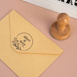 May include: A brown envelope with a round, black ink stamp that reads "Albert & Betty 02.12.2023" with a floral design and hearts.