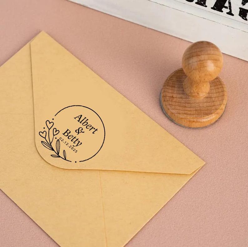 May include: A brown envelope with a round, black ink stamp that reads "Albert & Betty 02.12.2023" with a floral design and hearts.
