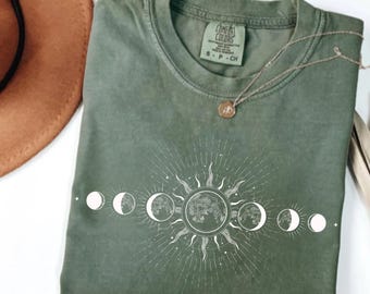May include: A green t-shirt with a white sun and moon phases design. The shirt has the text "COMFORT COLORS" and "S - P - CH" on the tag.