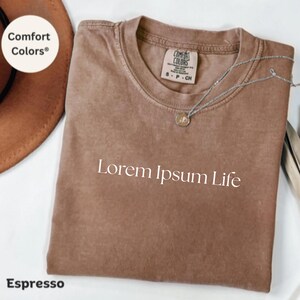 May include: Espresso brown t-shirt with the text "Lorem Ipsum Life" printed in white. The shirt is made of a soft, comfortable fabric and has a relaxed fit.